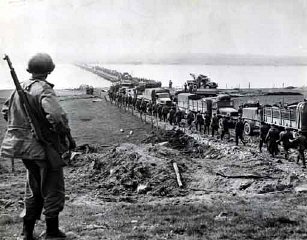 German prisoners file across the Rhine as American supply trucks move forward toward the front.