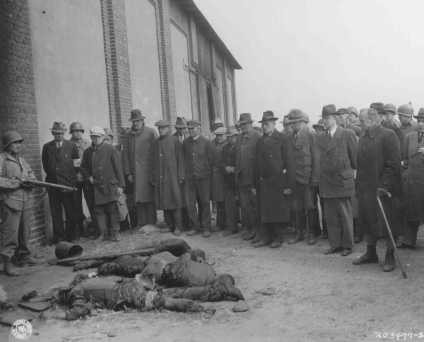 An American soldier stands guard as mayors and citizens of local towns view the corpses of inmates of the Rottleberode subcamp, who were killed when the SS locked them in a barn and set it on fire.