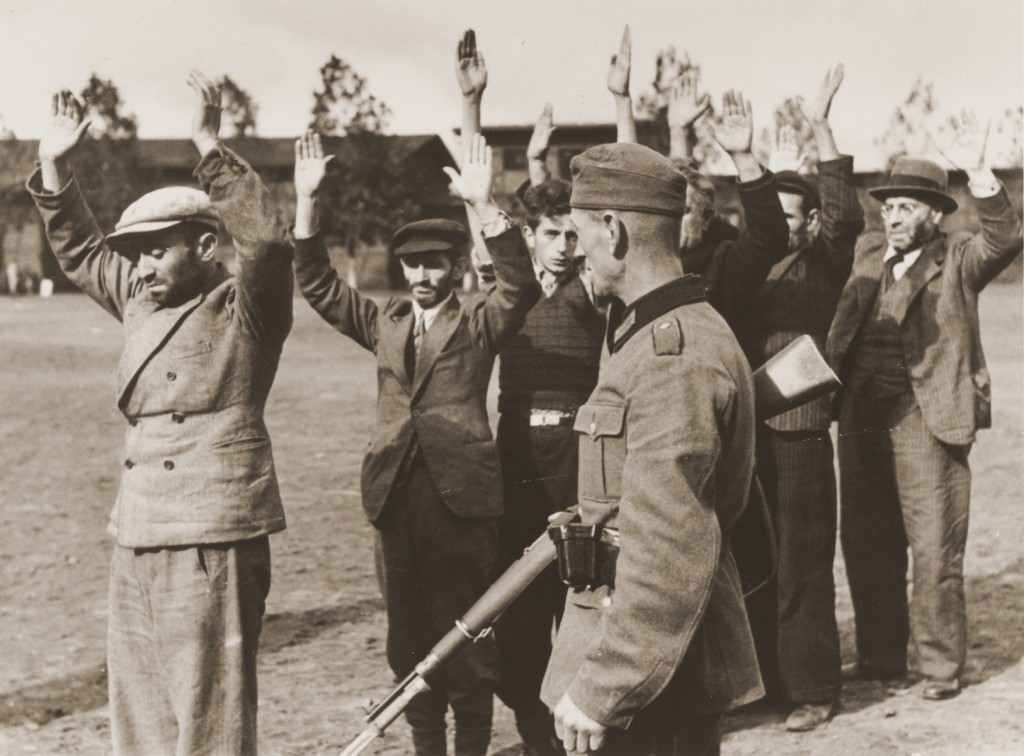 <p>A German soldier guards a group of Poles and Jews who have been rounded-up and forced to stand in a line with their arms raised, Poland, <a href="/narrative/2103">September 1939</a>. </p>