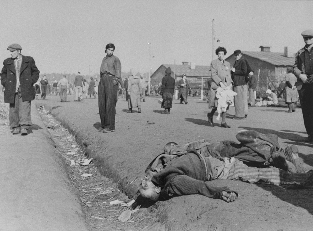 Soon after liberation, camp survivors walk amidst dead bodies. [LCID: 13053]