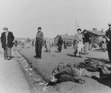 Soon after liberation, camp survivors walk amidst dead bodies. [LCID: 13053]