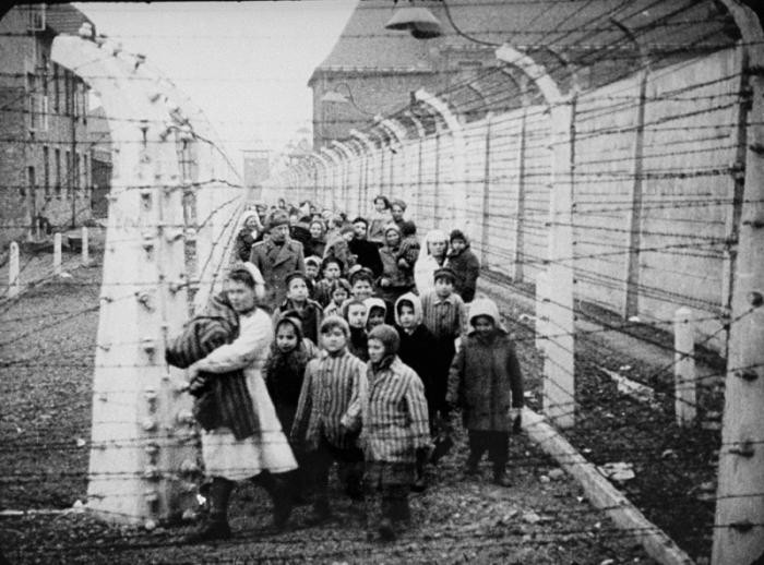 A large group of children and nurses stand in between barbed wire fences.