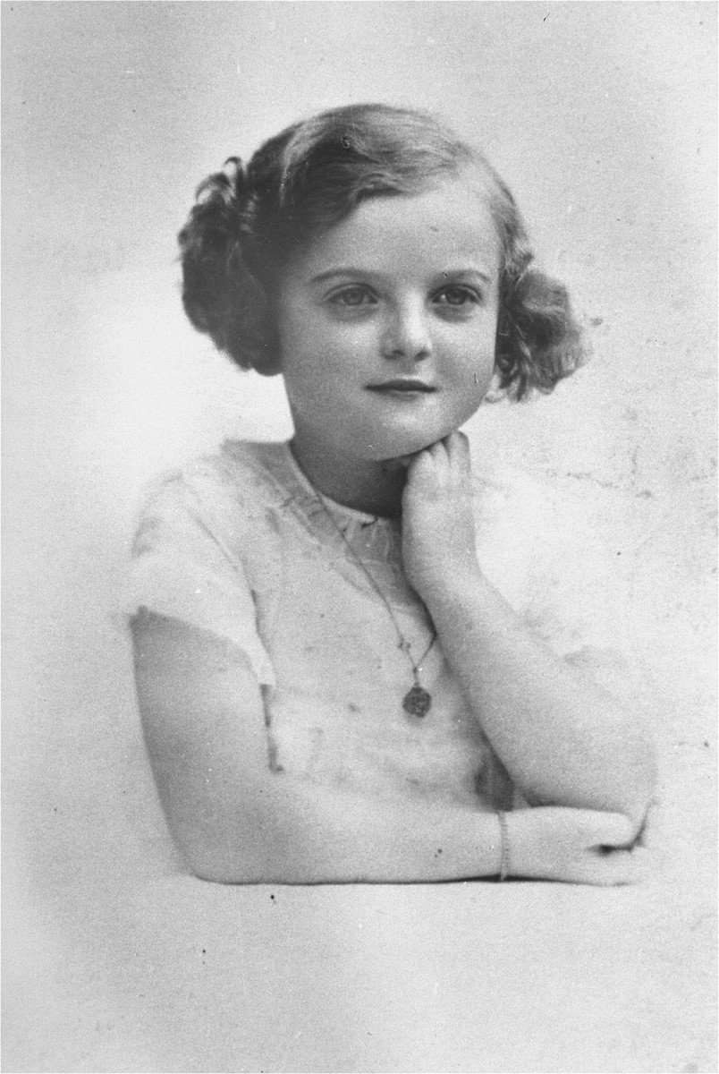 A young girl with light skin tone poses for the camera with one arm in front of her and the other propped up holding her head. Her hair is curled and pinned up. She is wearing a light colored dress with a medallion necklace.