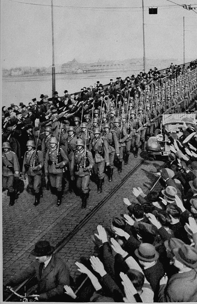 During the remilitarization of the Rhineland, German civilians salute German forces crossing the Rhine River in open violation of ...