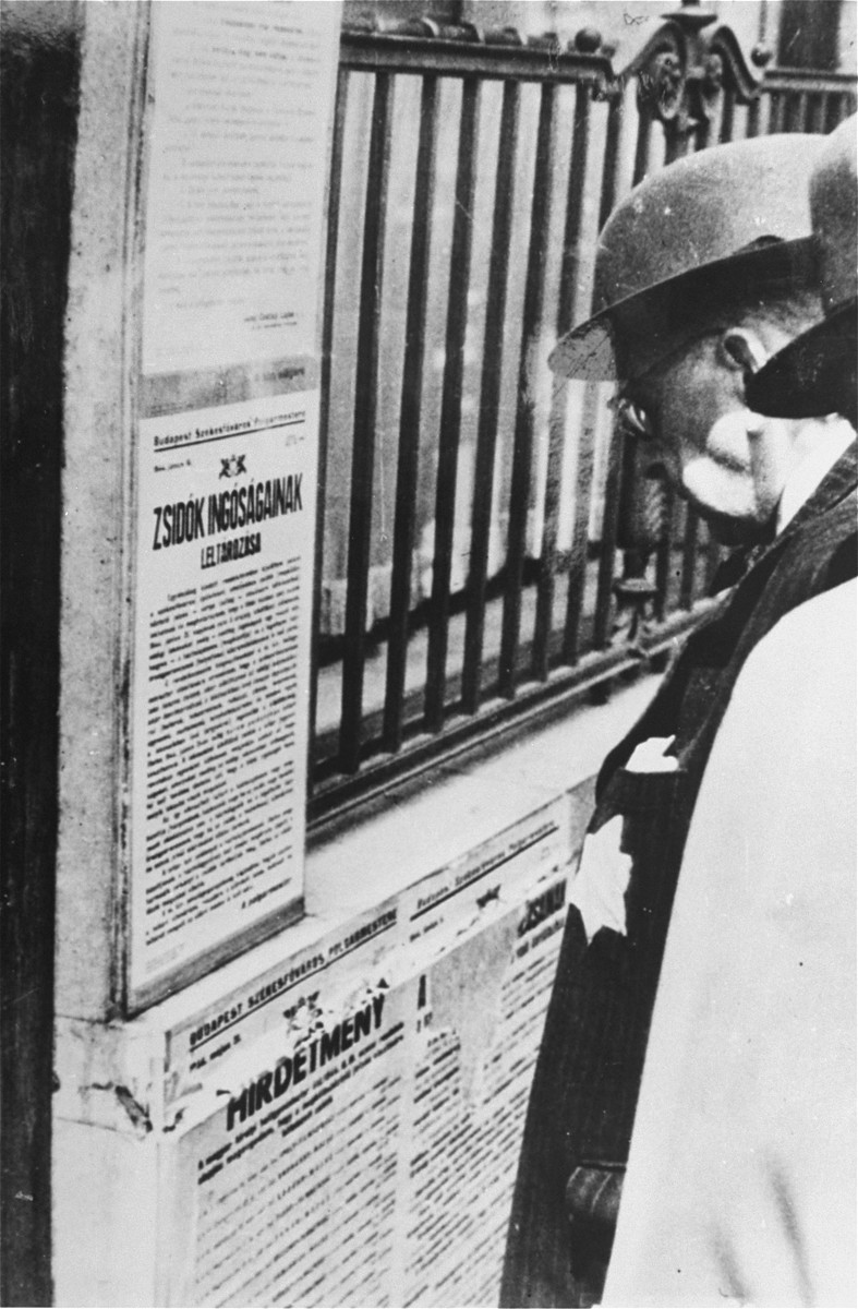 A Jewish man wearing a yellow star reads newly posted antisemitic regulations in Budapest. [LCID: 68612]