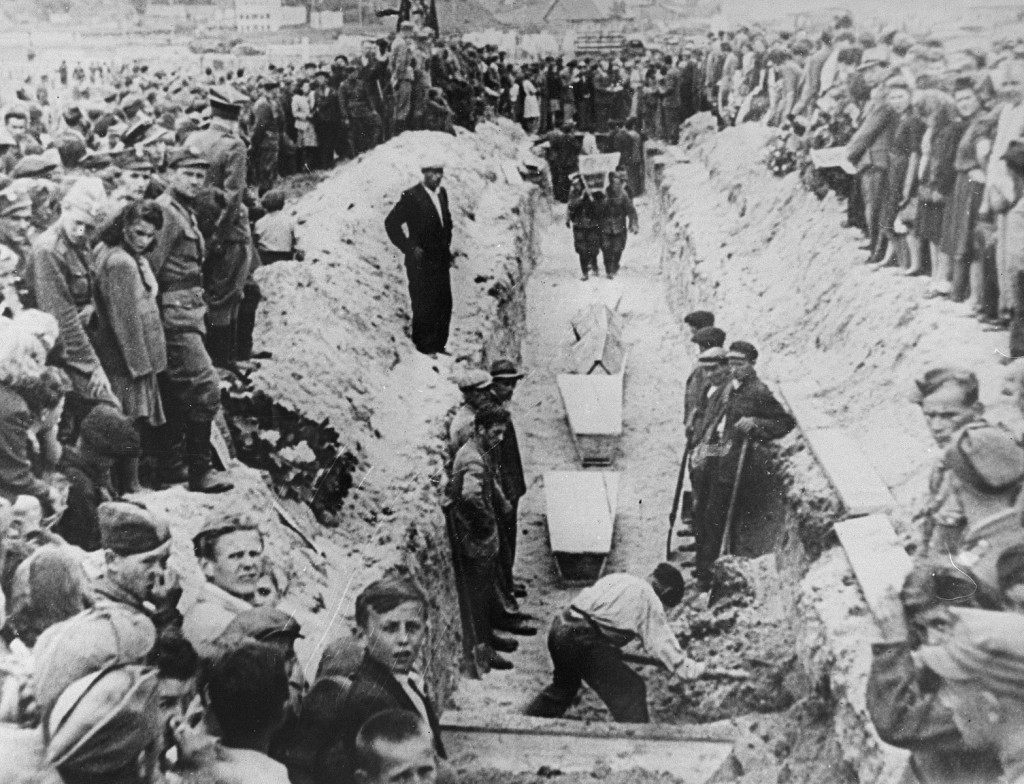 Mourners crowd around a narrow trench as coffins of pogrom victims are placed in a common grave, following mass burial service. [LCID: 85356]