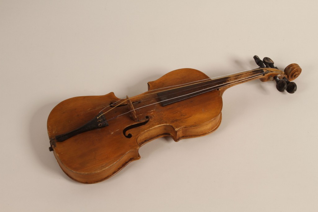 Light colored wooden violin. The instrument is missing one string and is worn with a few scratches.