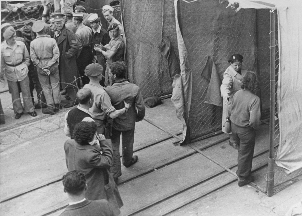 British soldiers force Jewish refugees from Aliyah Bet ("illegal" immigration) ship "Theodor Herzl" through a disinfection station ... [LCID: 69911]