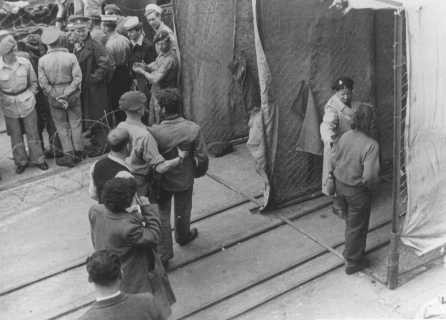 British soldiers force Jewish refugees from Aliyah Bet ("illegal" immigration) ship "Theodor Herzl" through a disinfection station ... [LCID: 69911]