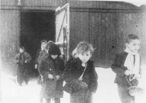 Soon after liberation, surviving children of the Auschwitz camp walk out of the children's barracks.