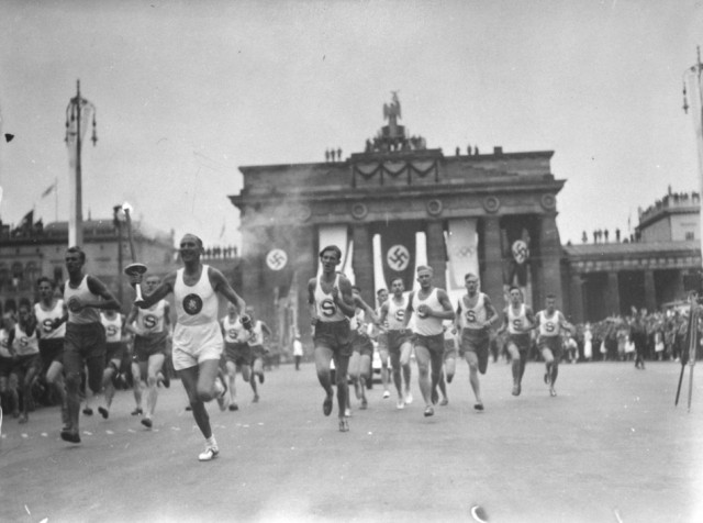 On August 1, 1936, Hitler opened the 11th Summer Olympic Games. Inaugurating a new Olympic ritual, a lone runner arrived bearing a torch carried by relay from the site of the ancient Games in Olympia, Greece. This photograph shows an Olympic torch bearer running through Berlin, passing by the Brandenburg Gate, shortly before the opening ceremony. Berlin, Germany, July-August 1936.