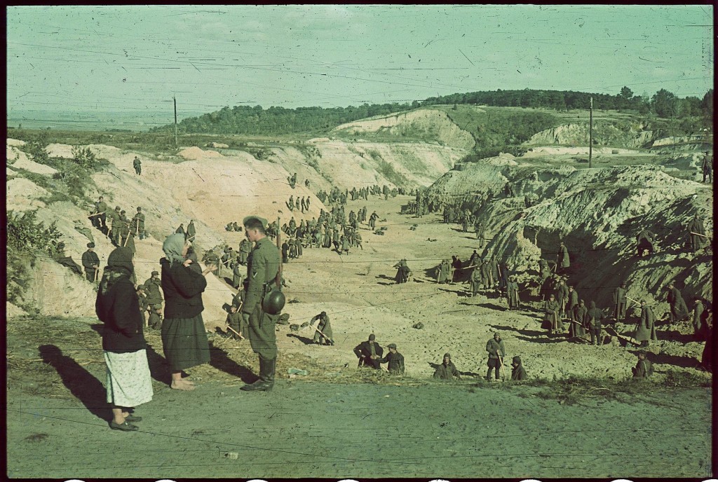 An SS guard speaks with local Ukrainian women while Soviet POWs perform forced labor nearby