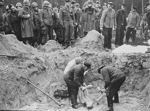 American troops with the 82nd Airborne Division look on as German exhume corpses from a mass grave.