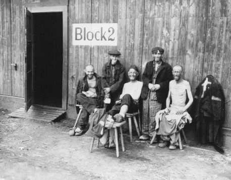 Five Jewish survivors pose for a US Signal Corps photographer in front of Block 2 in the Hanover-Ahlem camp, a subcamp of Neuengamme. [LCID: 0036]