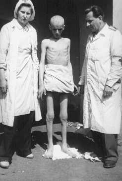 Shortly after liberation, an emaciated concentration camp inmate stands between two members of the International Red Cross. [LCID: 79465]