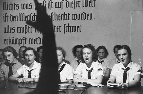 <p>German girls, members of a Hitler youth organization, follow their leader in song. The inscription behind them reads: "Nothing important in this world was given as a gift to people; everything must be struggled for." Berlin, Germany, 1938.</p>