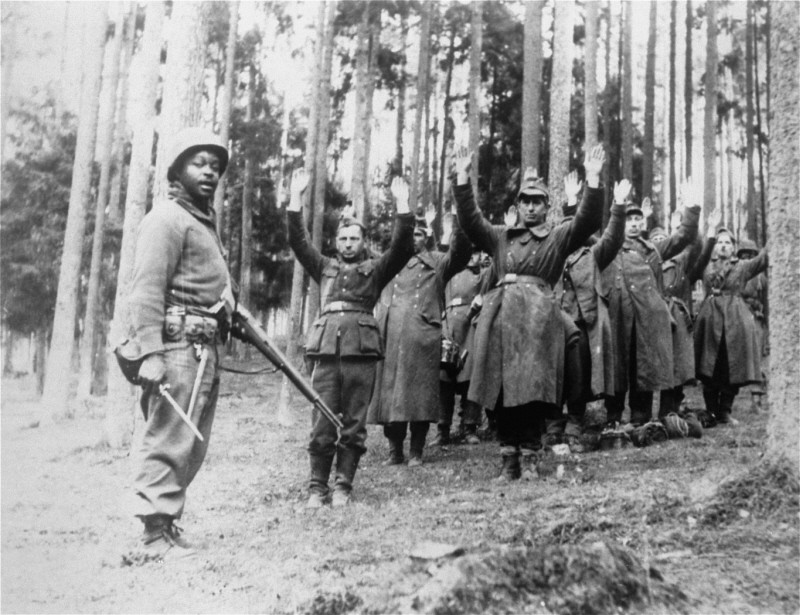 An African-American soldier stands guard over a group of captured German soldiers