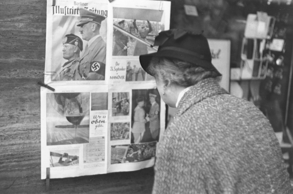 In Berlin, a German woman reads a copy of the Berliner Illustrierte newspaper, featuring photographs of Mussolini's official visit ...