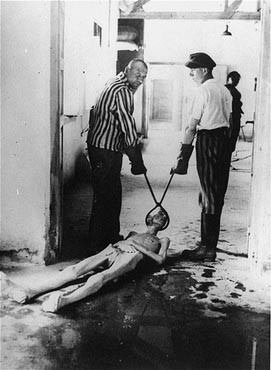 Survivors of the Dachau concentration camp demonstrate the operation of the crematorium by dragging a corpse toward one of the ovens.