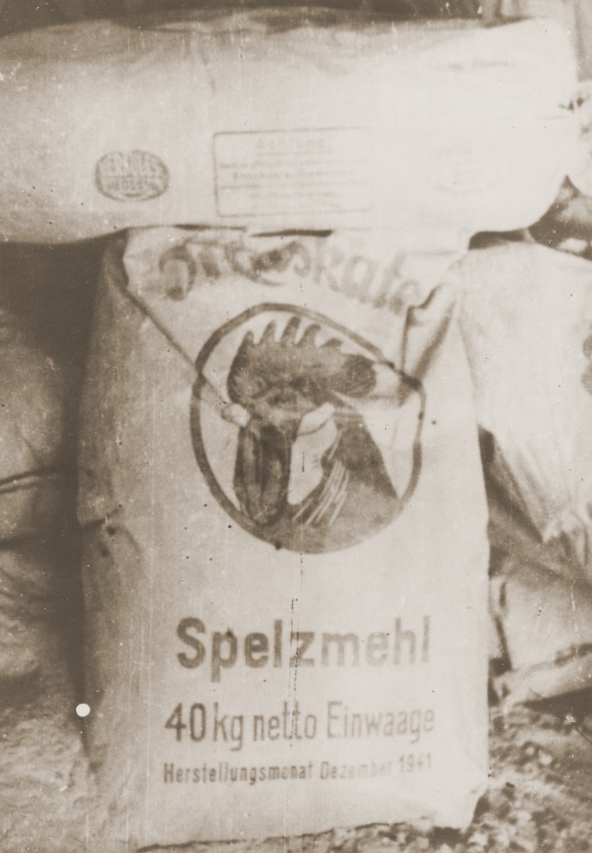Pile of large flour sacks. The sack features an illustration of the head of a rooster and German text.