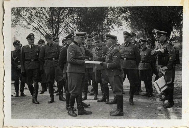 September 1, 1944, Richard Baer ceremonially accepts a copy of the construction plans from the Chief of the Central Construction Directorate of the Waffen SS, SS-Sturmbannführer Karl Bischoff, celebrating the opening of an SS military hospital (SS-Lazarette).