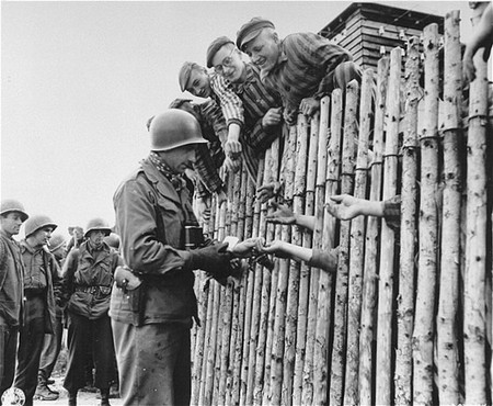 Un soldat américain offre des cigarettes à des détenus du camp de concentration de Dachau fraîchement libérés. [LCID: 71051]