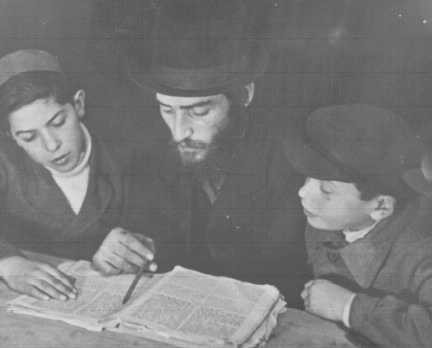 <p>A Jewish refugee teacher instructs children in religious law from the Talmud. Landsberg displaced persons camp, Germany, after 1945.</p>