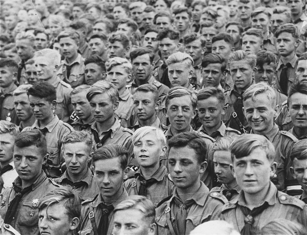 A large crowd of young men wearing uniforms with a collared shirt and neck tie. Most of them have light hair and light to medium skin tones and are visible from the neck up.