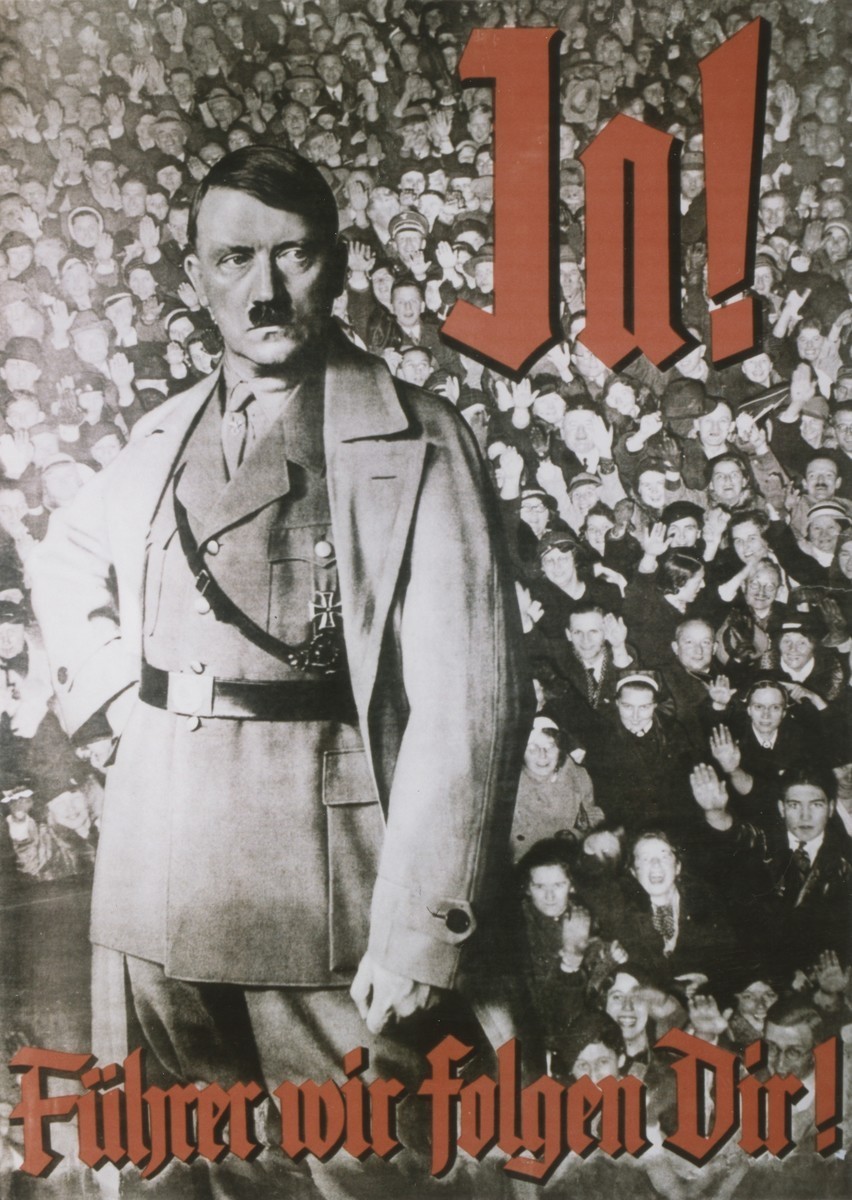 Adolf Hitler stands defiantly looking off to the side, with a crowd of adoring supporters behind him in the distance. In the top right corner, large red letters saying ‘Ja!’ contrast brightly against the black and white of the rest of the poster. The rest of the text is along the bottom.