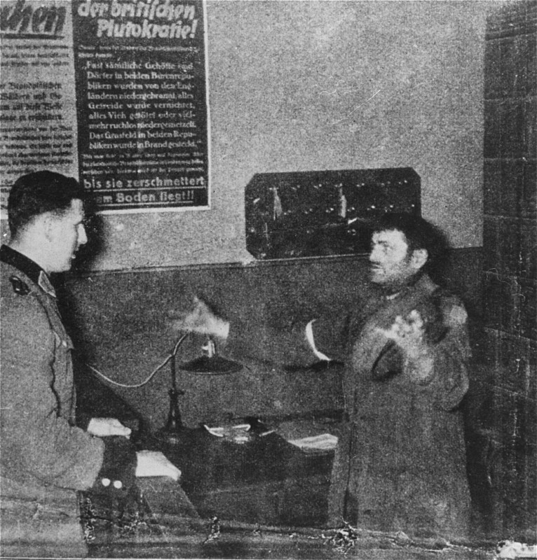 A German policeman interrogates a Jewish man accused of trying to smuggle a loaf of bread into the Warsaw ghetto.