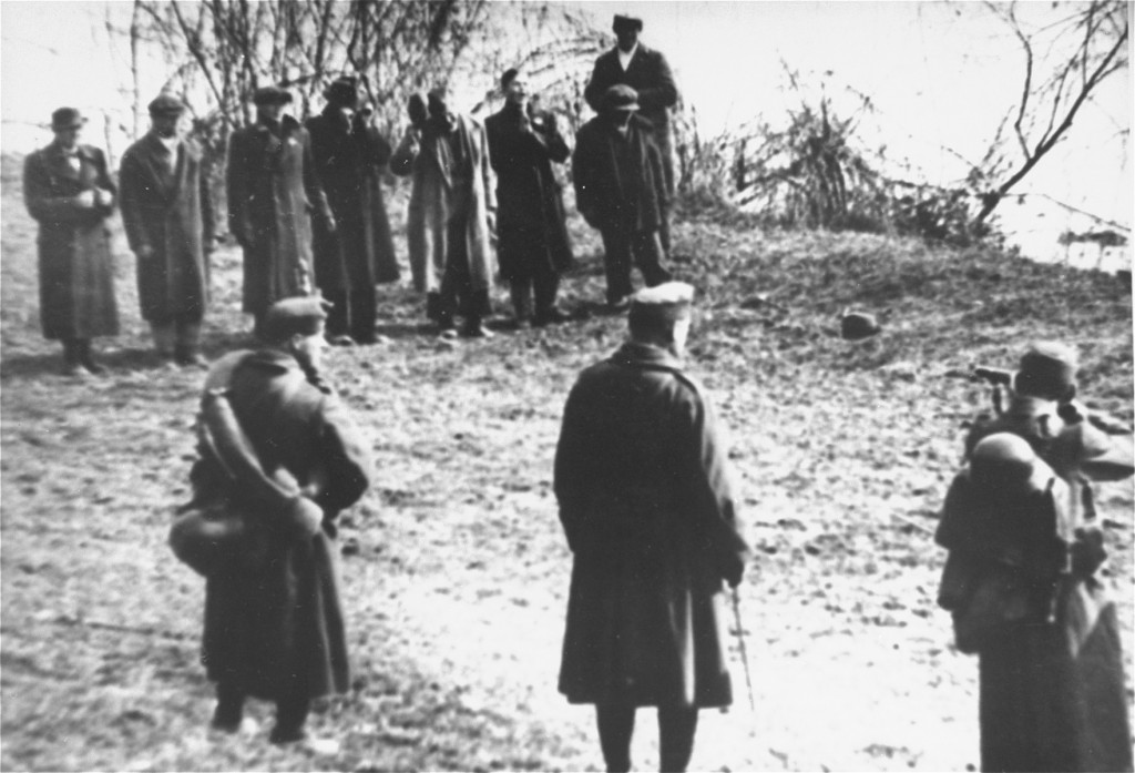 Three uniformed people stand across a field ready to fire upon a line of eight people in heavy outerwear.
