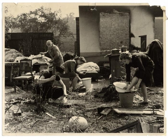 Members of a Polish family perform daily chores amidst the amidst the charred ruins of their home, destroyed during the German bombing of Warsaw. They have reassembled the remnants of their household furnishings outside. Photographed by Julien Bryan, circa 1939.