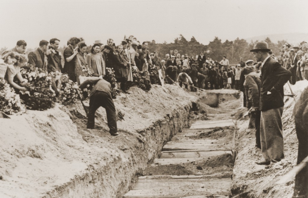 Mourners and local residents shovel dirt into the mass grave of the victims of the Kielce pogrom during the public burial. [LCID: 14390]