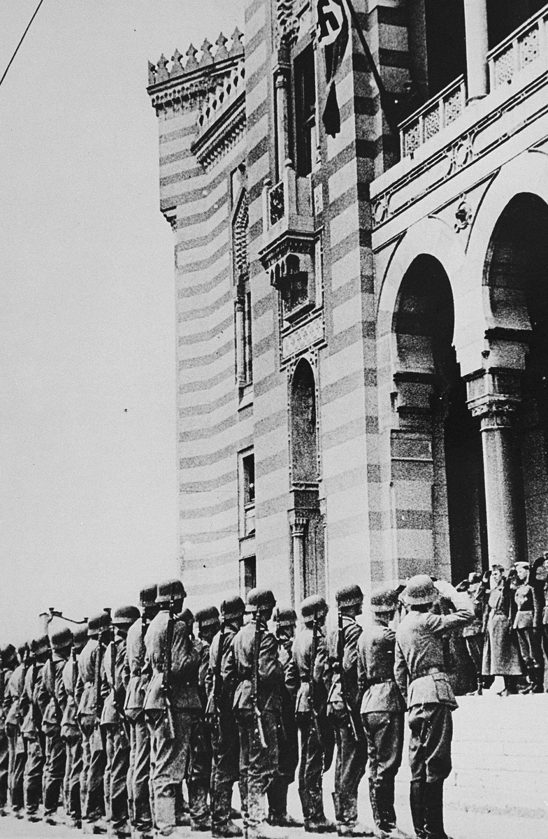 A flag bearing a swastika is raised over the city hall in Sarajevo after German forces captured the city. [LCID: 20359]
