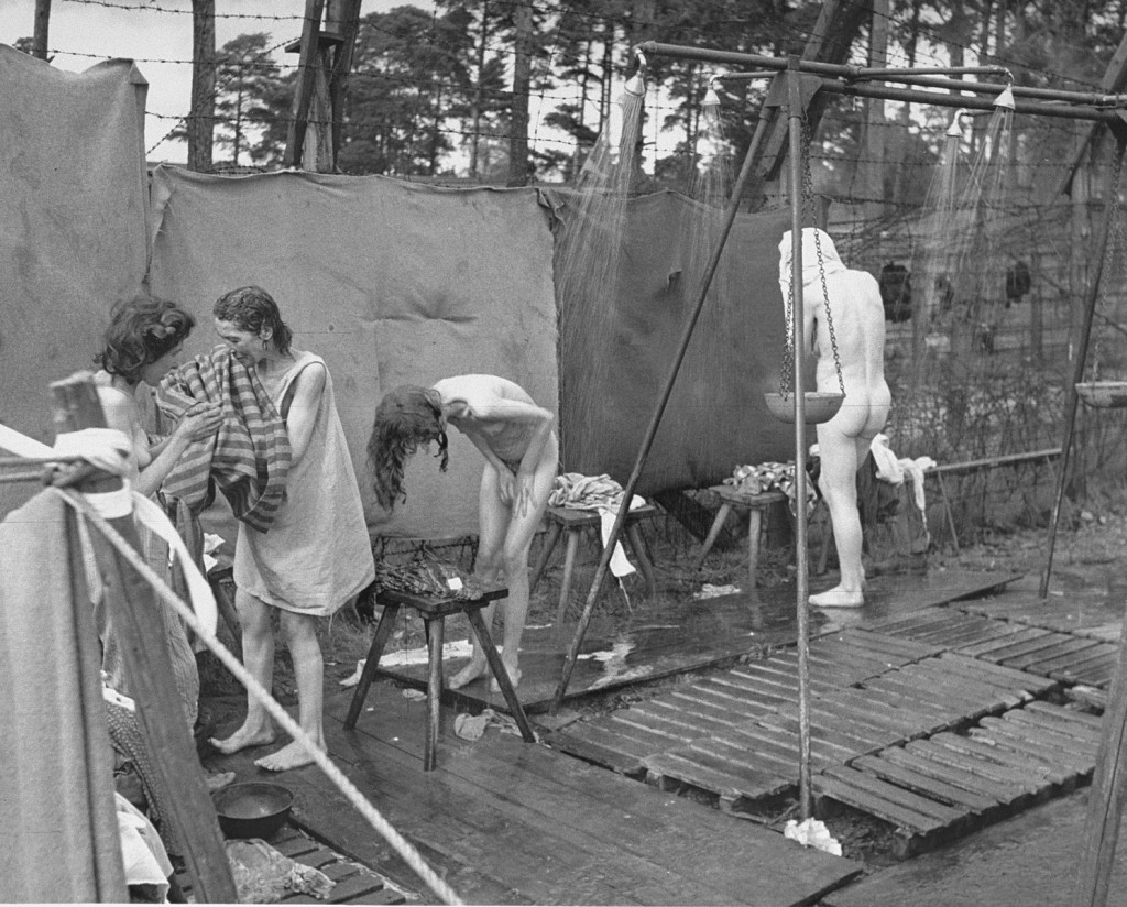 Soon after liberation, camp survivors bathe in outdoor showers set up by the British. [LCID: 45050]