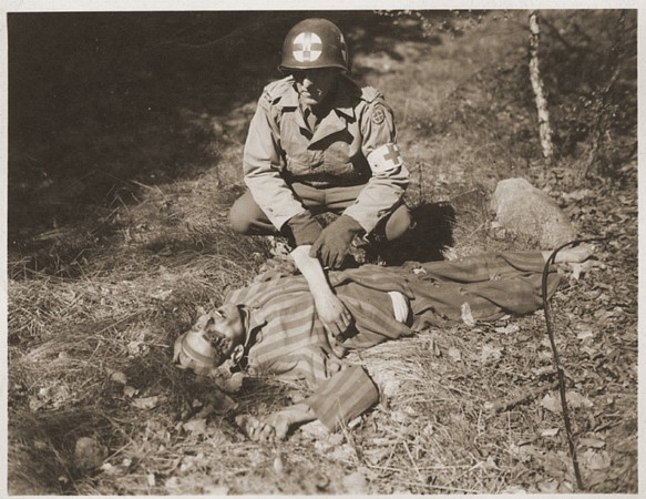 An American soldier kneels by the corpse of a prisoner on the roadside near Gardelegen.