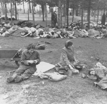 Soon after liberation, women camp survivors prepare food near piles of dead bodies. [LCID: 32080]
