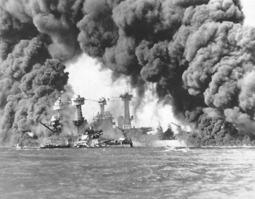 Smoke fills the background as military ships burn and sink in Pearl Harbor.