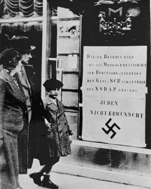 Viennese pedestrians view a large Nazi sign posted on a restaurant window informing the public that this business is run by an organization of the Nazi party and that Jews are not welcome.
