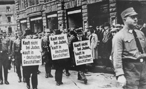 Three Jewish businessmen are forced to march down a crowded Leipzig street while carrying signs reading: "Don't buy from Jews. Shop in German businesses!" Leipzig, Germany, 1935.