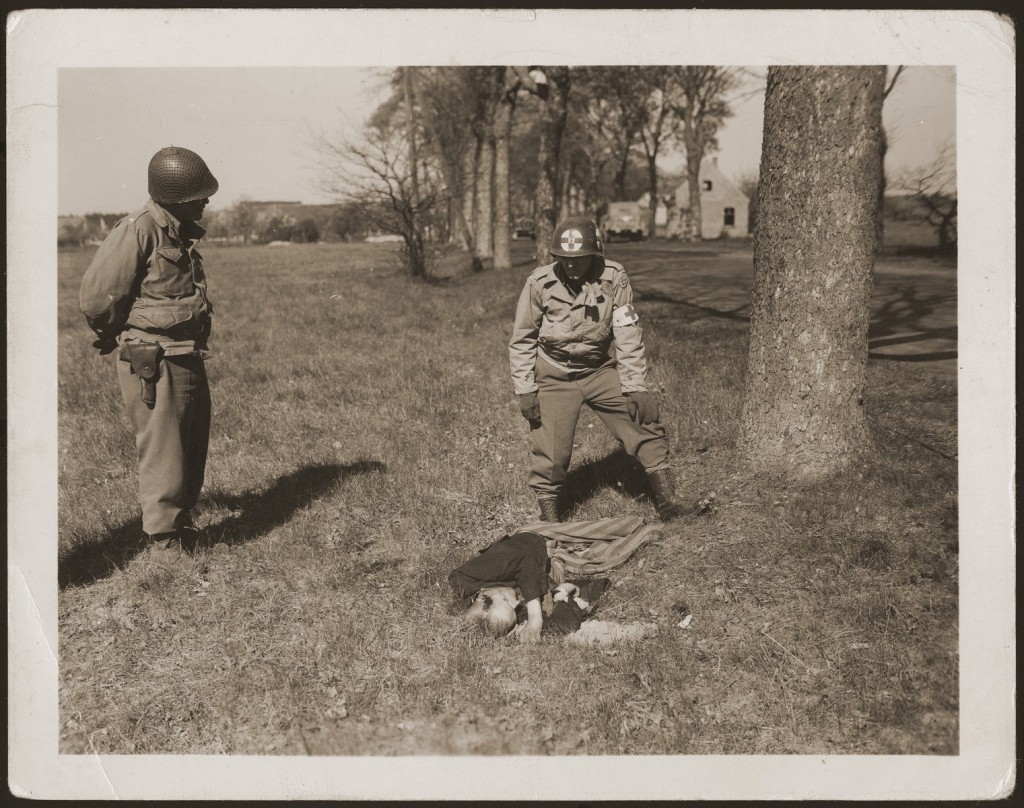 An American medic and soldier stand by the corpse of a prisoner shot on the road near Gardelegen. [LCID: 28196]