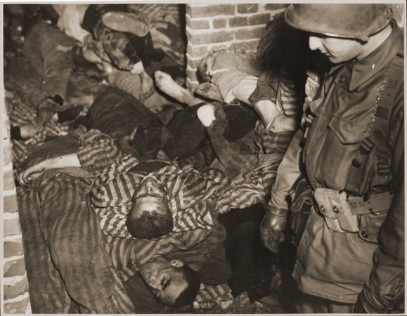 An American soldier views the bodies of prisoners piled on top of one another in the doorway of a barracks in Wöbbelin.