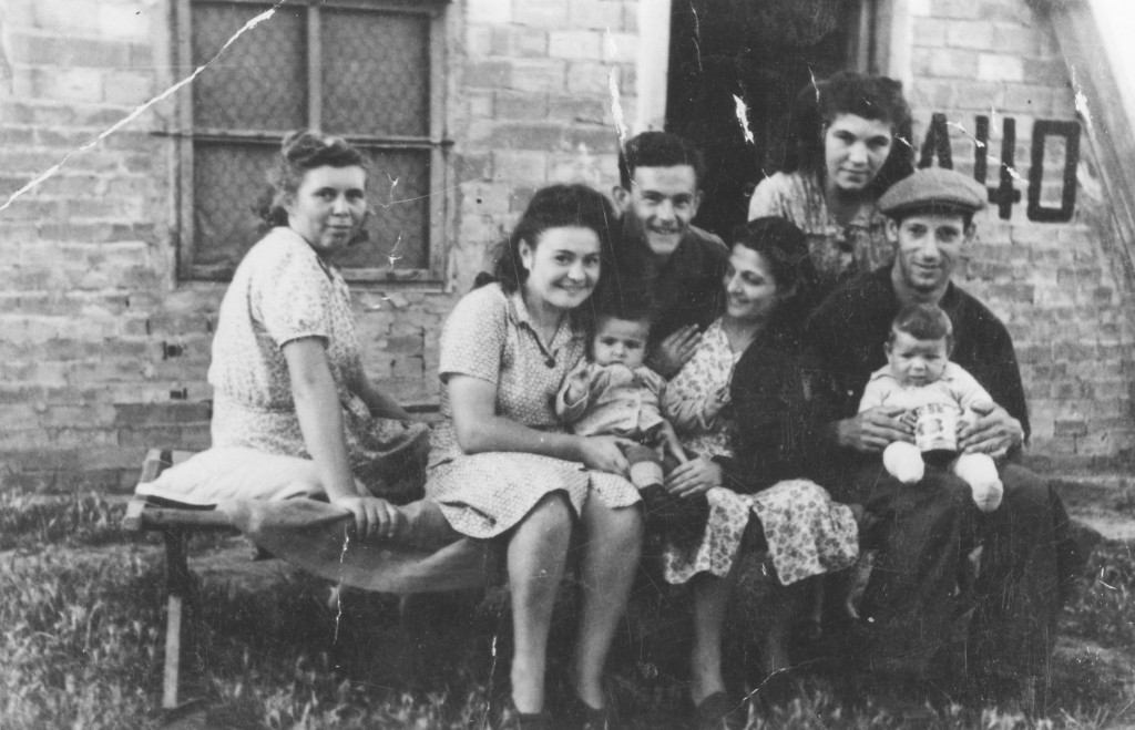 Jewish displaced persons (DPs) pose outside of a barracks in the Bari Transit DP camp in Italy. Among those pictured are Izidor and Tauba Schachter with their baby Miriam Schachter (now Enright), on the far right, and Etta Gipsman, on the far left.  