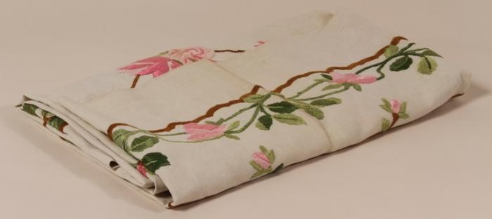 Tablecloth with roses embroidered by her mother carried by 17 year old Hannah Kronheim when she left Germany on the Kinderstransport [Children's Transport] in 1939.