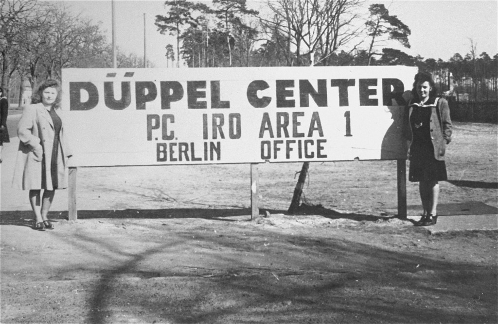 Displaced persons (DPs), Lusia Gliklich (left) and Andzia Dell, stand beside the sign in front of the Düppel Center DP camp, also called Schlachtensee.