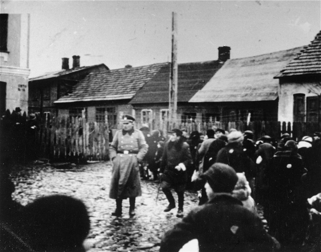 A German police officer stands in a fenced-in yard among a group of Jews, who have been rounded-up in the Ciechanow ghetto. [LCID: 50339]
