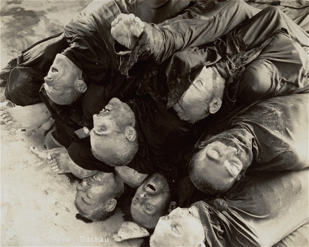 A pile of corpses, wrapped in fabric from the neck down. The faces and feet of the victims can be seen.