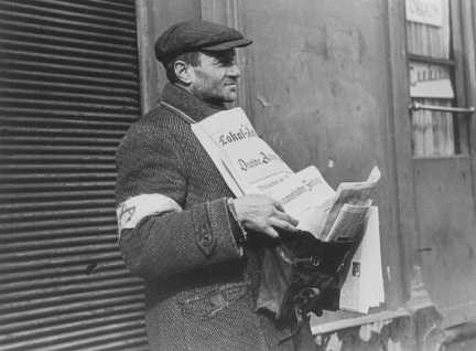 <p>A Jewish street vendor, wearing the compulsory armband, sells German-language newspapers. Warsaw ghetto, Poland, February 1941.</p>