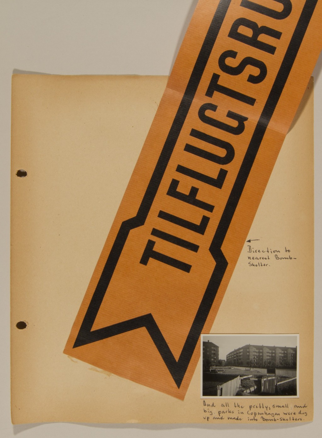 Scrapbook page with handwritten notes in black ink. A large orange sign with an arrow is pasted in the center with a small photograph in the bottom right corner.