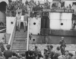 イギリス海軍の海域封鎖の強行突破に失敗した難民船「テオドール・ヘルツル」号の船上で殺された難民の（ユダヤ国旗で覆われている）遺体を船から降ろすイギリス兵たち。 1947年4月14日、パレスチナ、ハイファ港。